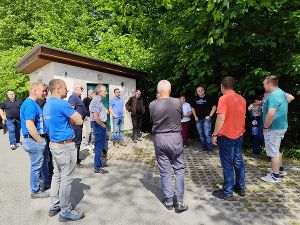 Gruppe von Menschen steht im Freien vor einem kleinen Gebäude und führt ein Gespräch.
